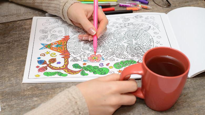 Woman coloring an adult coloring book and drinking tea